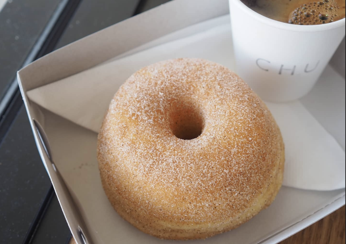 A large cinnamon donut and coffee sits in a paper tray from Chu Bakery